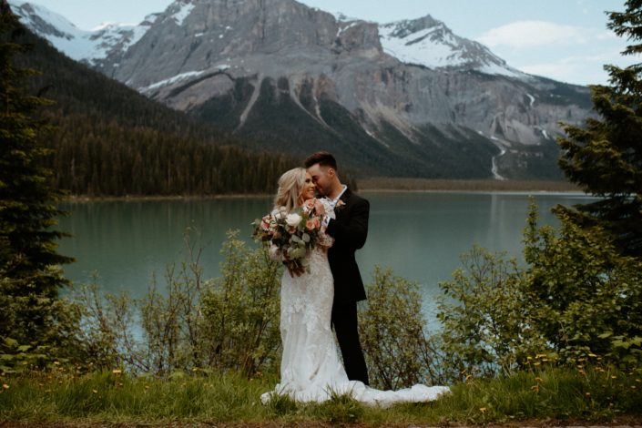 Bride and groom with bridal bouquet alongside Emerald Lake with a view of the Rocky Mountains