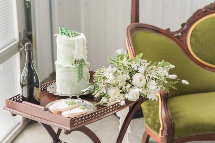 Drink cart covered with champage, cake, and green and white bridal bouquet featuring poppies, ranunculus, veronica, astilbe, sweet peas, bunny tails, wax flower and greenery.