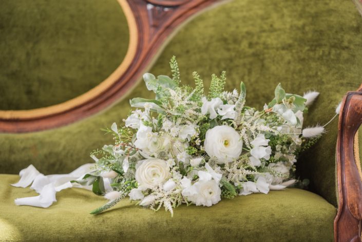 White and green romantic bridal bouquet designed with white flowers such as poopies, ranunculus, astilbe, veronica, wax flower, bunny tail and sweet peas with a mixed variety of greenery.