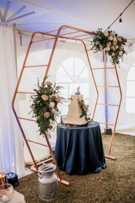 Copper hexagon decorated with mauve and navy floral arrangements with a flower covered wedding cake