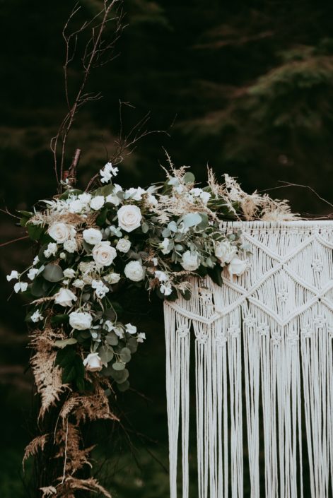 Natural white and green wedding woven twig archway decorated with macrame and a corner arrangement made of white astilbe, ranunculus, Tibet roses, spray roses, sweet peas, Italian ruscus, eucalyptus and gold plumosa