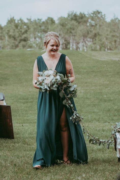 Bridesmaid wearing green floor-length gown while holding natural white and green bouquet and walking dog with eucalyptus garland leash