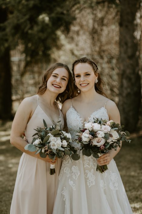 Bride wearing white lace gown and bridesmaid wearing blush gown holding blush, white and burgundy bouquets