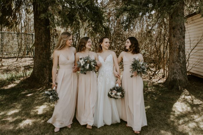 Bride with bridesmaids wearing blush floor length dresses and holding blush, white and burgundy bouquets