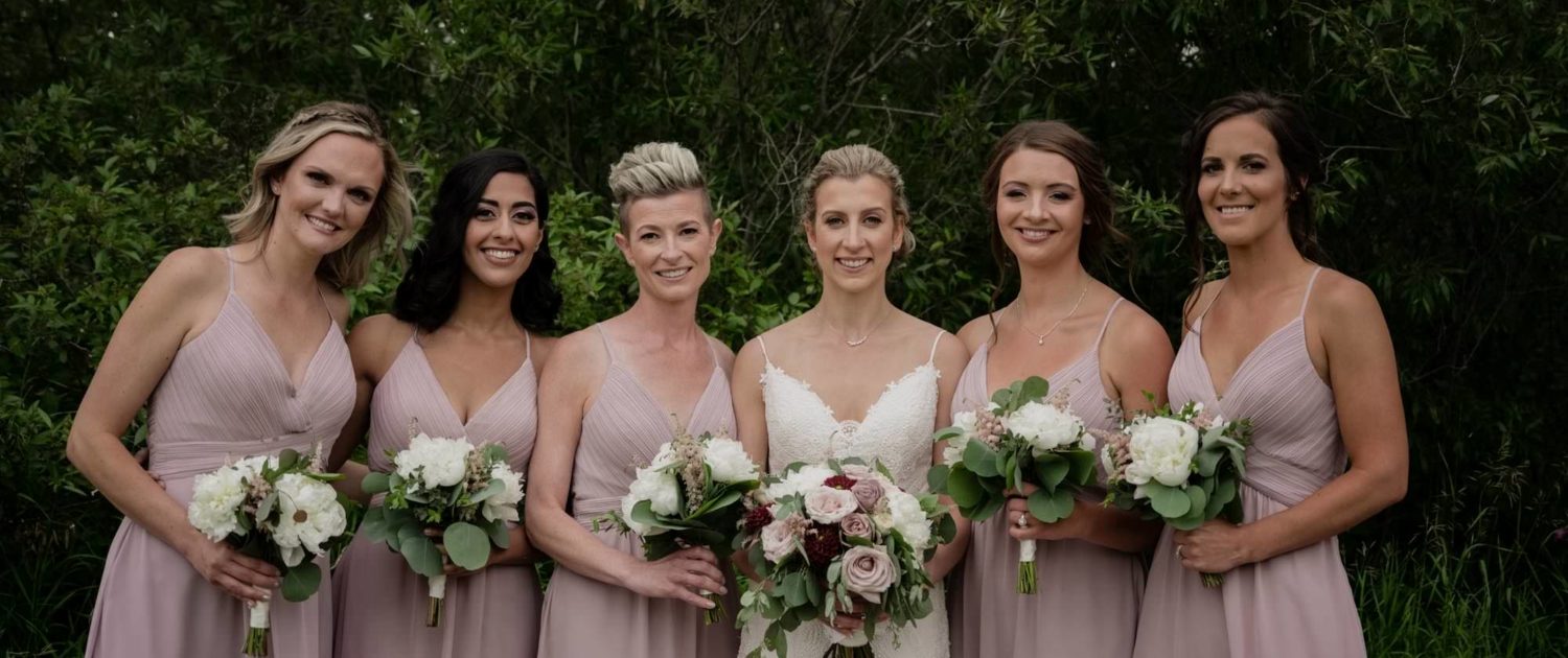 Burgundy and Mauve bride and bridesmaids; bridesmaids wearing mauve dresses and carrying white and blush bouquets designed with astilbe, peonies and eucalyptus; bride carrying white, blush, mauve and burgundy bouquet designed with dahlias, quicksand roses, ranunculus, peonies, amnesia roses, astilbe and eucalyptus