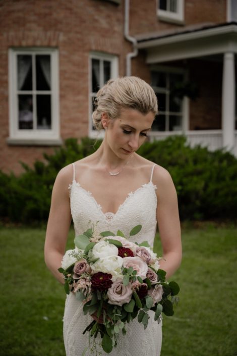 Bride looking at burgundy and mauve bridal bouquet featuring dahlias, peony, ranunculus, amnesia roses and quicksand roses.