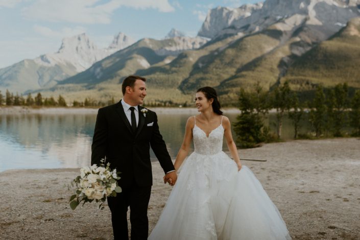 Bride and groom walking by a mountain lake with white bridal bouquet