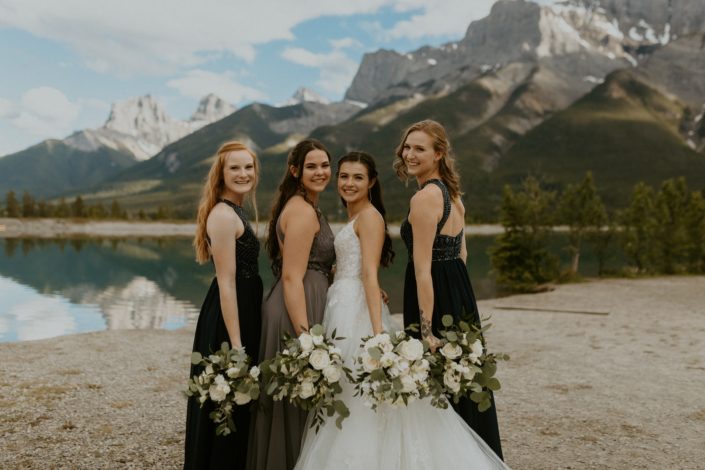Bride and bridesmaids holding white bouquets in the mountains; bouquets included roses, ranunculus, lisianthus