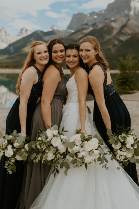 Bride and bridesmaids wearing white, grey and navy with white bouquets designed with roses, ranunculus, lisianthus and sweet peas