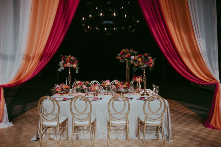 Bold Fuchsia and Orange table with drapery, tall arrangements, compote arrangements with accents of gold