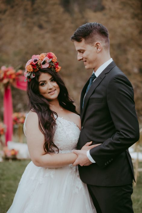 Bride and groom with colourful fuchsia and orange flower crown made of anemones, zinnias, and roses