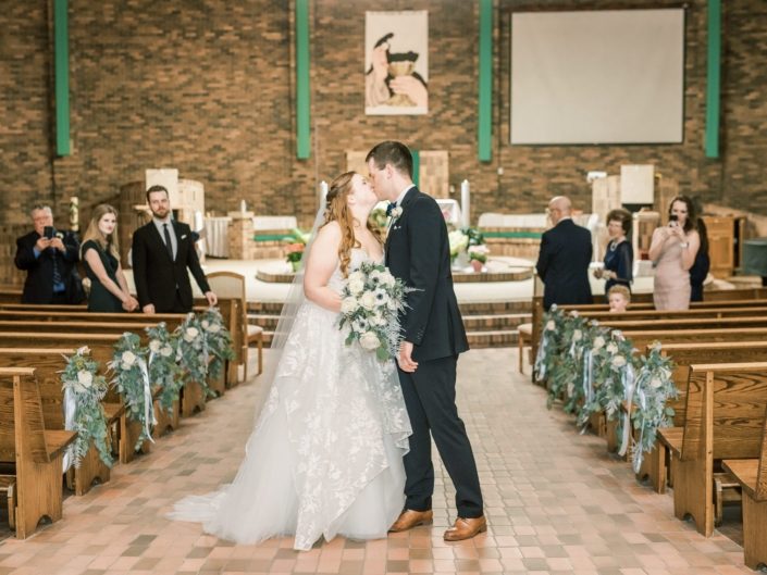 Bride and groom kissing while walking up aisle with white and silver bouquets surrounded by aisle markers