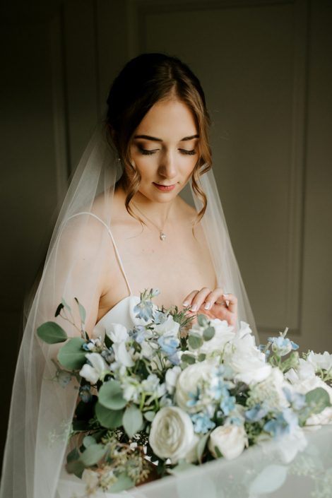 Bride, Erin, with white and blue bridal bouquet designed with delphinium, eryngium, forget me not, white cloud garden rose, ranunculus, sweet pea and eucalyptus greenery