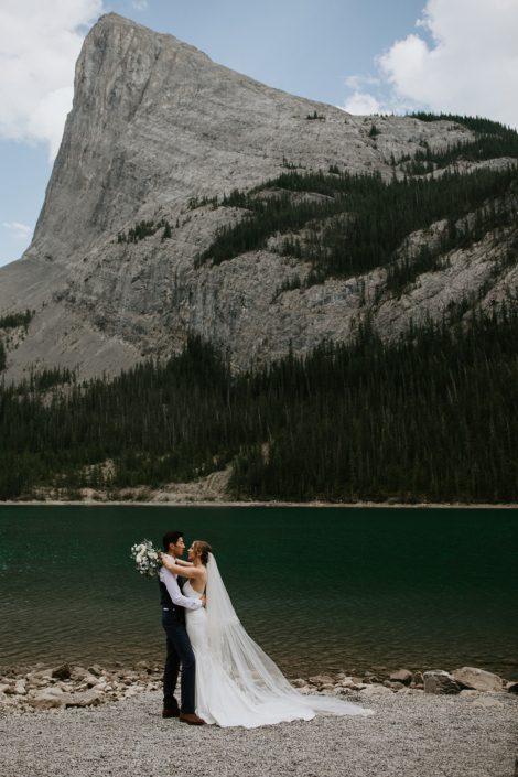 Bride and groom kissing near Canmore Rocky Mountains with white and blue bridal bouquet