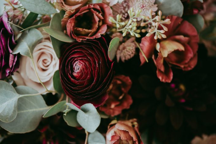 Rustic burgundy and dusty rose wedding flowers close up; ranunculus, lisianthus, quicksand roses, astrantia and seeded eucalyptus