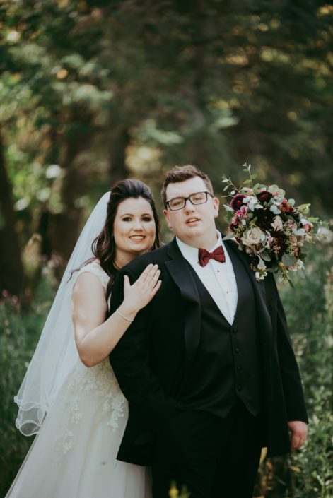 Bride and groom with rustic burgundy and dusty rose bridal bouquet featuring roses, dahlias and ranunculus
