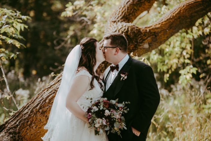Kaylee and Mitch kissing with burgundy and dusty rose bridal bouquet and boutonniere