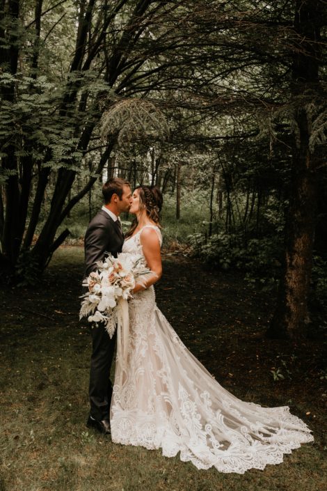 blush and white Rustic Boho Bride and Groom kissing in the woods with blush and white bridal bouquet