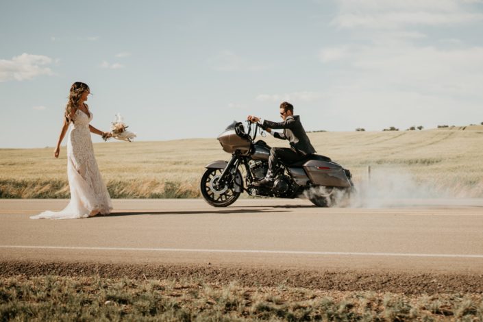 Bride and groom on a highway with motorcycle and rustic boho bridal bouquet