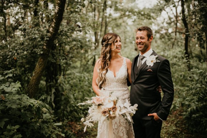 Bride and groom with rustic boho bridal bouquet and boutonniere; bouquet designed with roses, ranunculus, phalenopsis orchids, bleached bracken fern, bunny tail, astilbe, olive branches and eucalyptus
