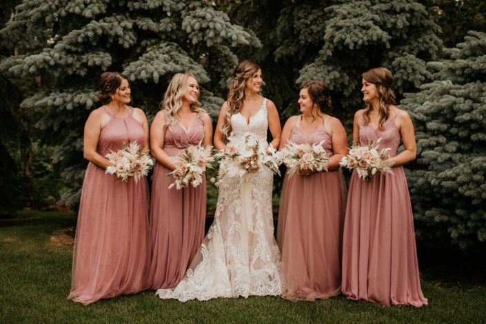 Bride and bridesmaids wearing dusty mauve with rustic boho bouquets designed with quicksand roses, amnesia roses, blush ranunculus, phalenopsis orchids, light pink astilbe, bleached bracken fern, bunny tail, eucalyptus cinerea, and olive branches