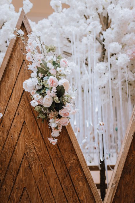 Wooden mountain backdrop decorated with an arrangement of white, peach and pink artificial flowers