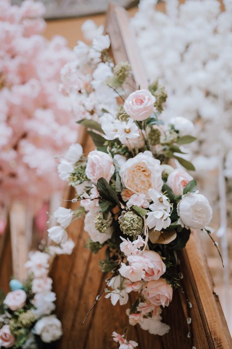 White, peach, pink and green artificial botanicals at the top of the wooden mountains backdrop