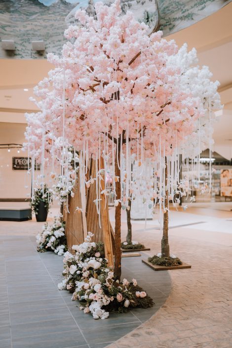 Artificial pink tree with Easter eggs hanging from it and artificial flowers at the base