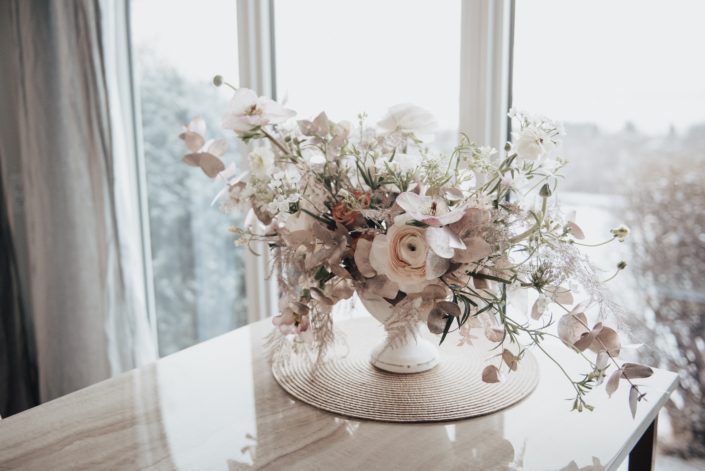 Flower arrangement featuring blush ranunculus, hellebores, rose gold plumosa, rose gold painted eucalyptus, roses, white allysum