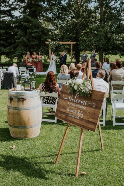 Rusty Rose Wedding at Hilltop Outdoor Ceremony featuring welcome sign with floral piece, lanterns and archway arrangement