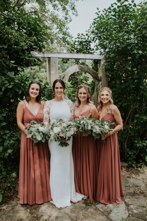 Bride with bridesmaids wearing white and rusty rose dresses, carrying white, ivory and blush bouquets