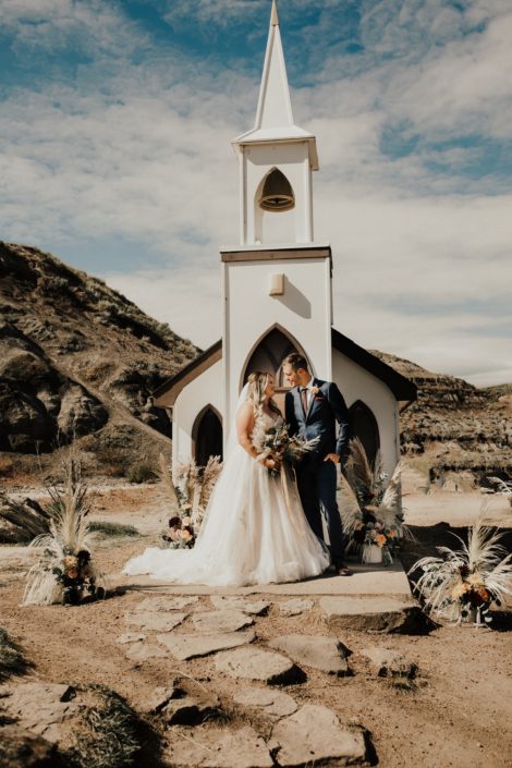 Bride and groom in front of a church in Drumheller with boho floral arrangements