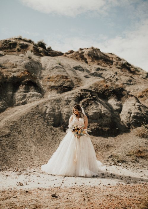 Boho Bride, Lizelle, in the Drumheller desert with peach and burgundy boho bouquet