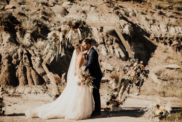 Bride and groom kissing in Drumheller desert with boho bridal bouquet