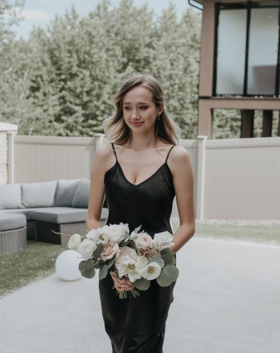 Bridesmaid wearing black and carrying a white, pink and yellow pastels bouquet designed with astilbe, patience garden roses, blush peonies, poppies, ranunculus, quicksand roses and eucalyptus greenery