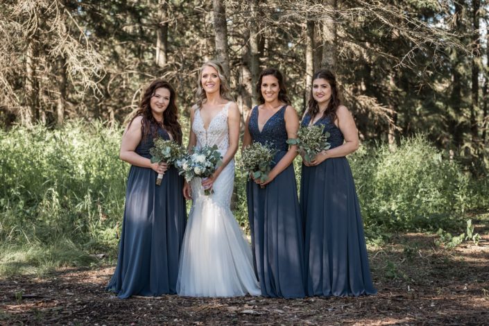 Bride with bridesmaids wearing blue floor length gowns and carrying greenery bouquets and blue and white bridal bouquet