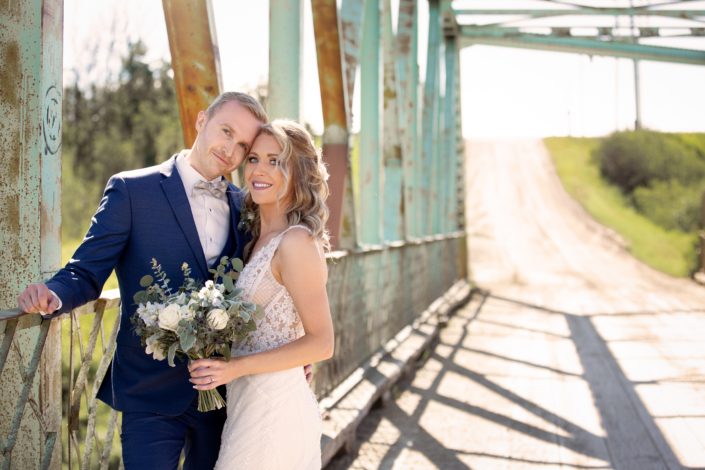 Bride and groom under a blue bridge with a blue and white bridal bouquet featuring panda anemones, ranunculus, roses, eryngium, and delphinium