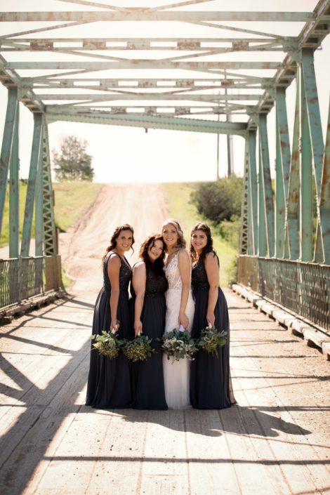 Bride with bridesmaids wearing blue dresses with white and blue bridal bouquet and greenery bridesmaids bouquets under a blue bridge
