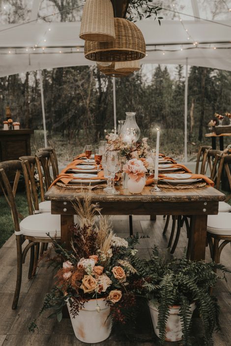 Intimate wooden table decorated with natural elements such as terracotta pots, rust coloured napkins, woven basket decor, ferns, pottery and ceramics