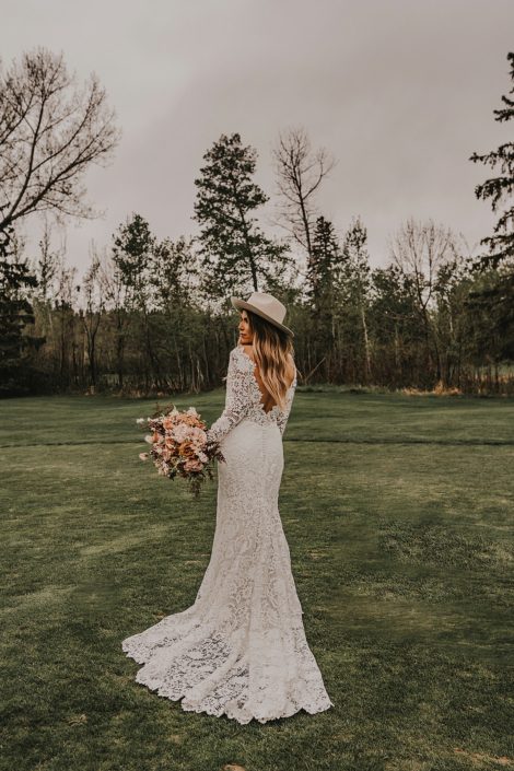 Modern boho bride wearing a lace gown and a boho hat with terracotta, rust and blush toned flowers