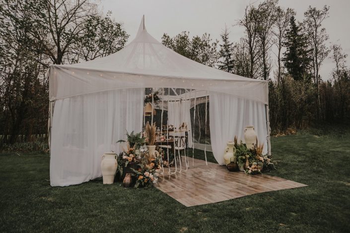 Small white tent decorated with pottery and boho decor with ferns, pampas grass and rust coloured flowers