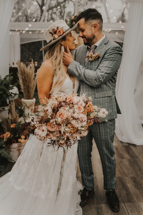 Modern Boho and Terracotta Couple with bridal bouquet, hat flowers and boutonniere; featured rust coloured flowers such as roses, cosmos, lisianthus and sweet peas