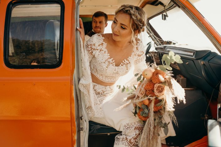 Boho bride with orange bridal bouquet in an orange van