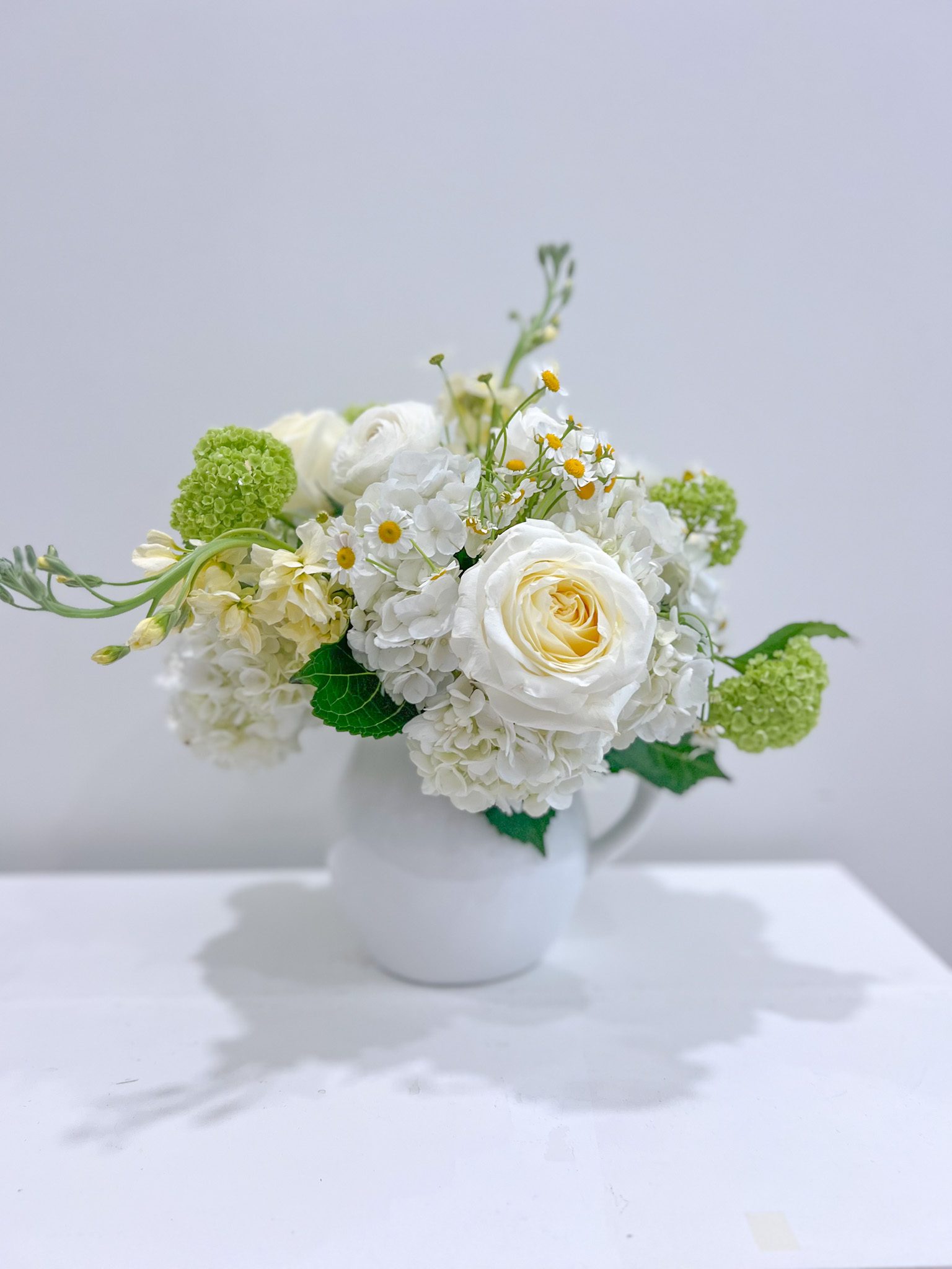A full arrangement in white, crisp green and pale yellows designed into a jug vase.
