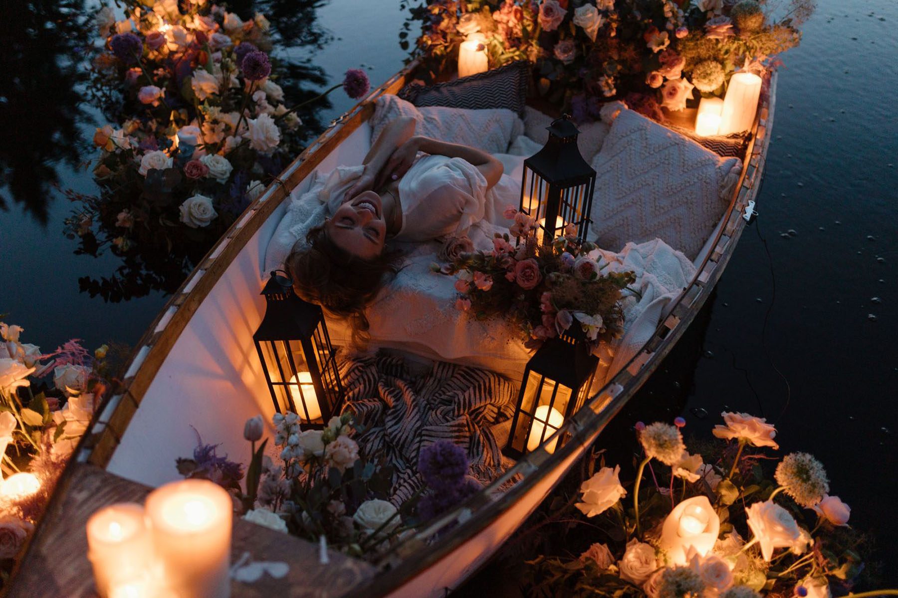 Woman lying in canoe on a candlelit lake surrounded by floral arrangments