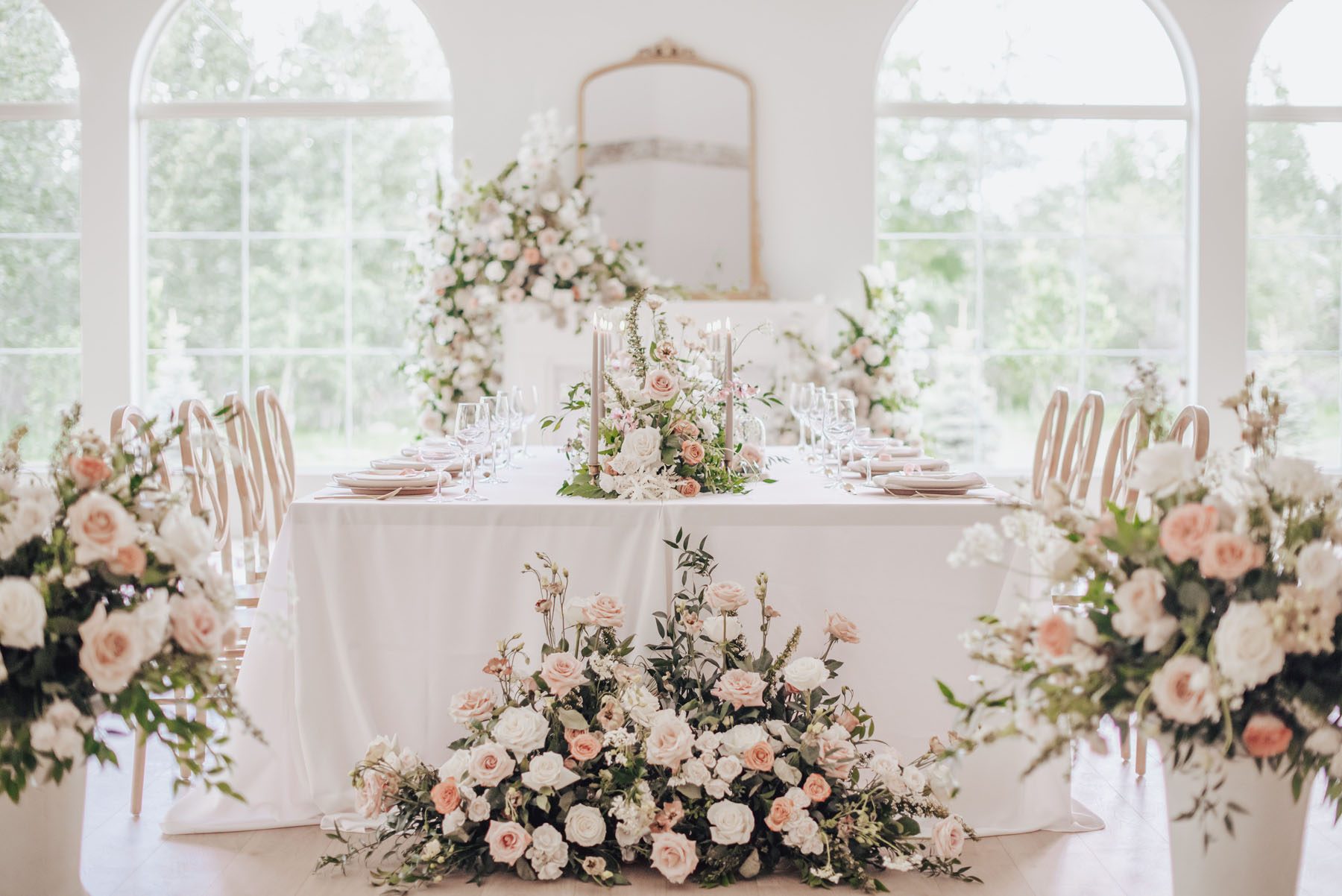 White wedding table with pink centerpieces and surrounding blush, pink and green arrangements