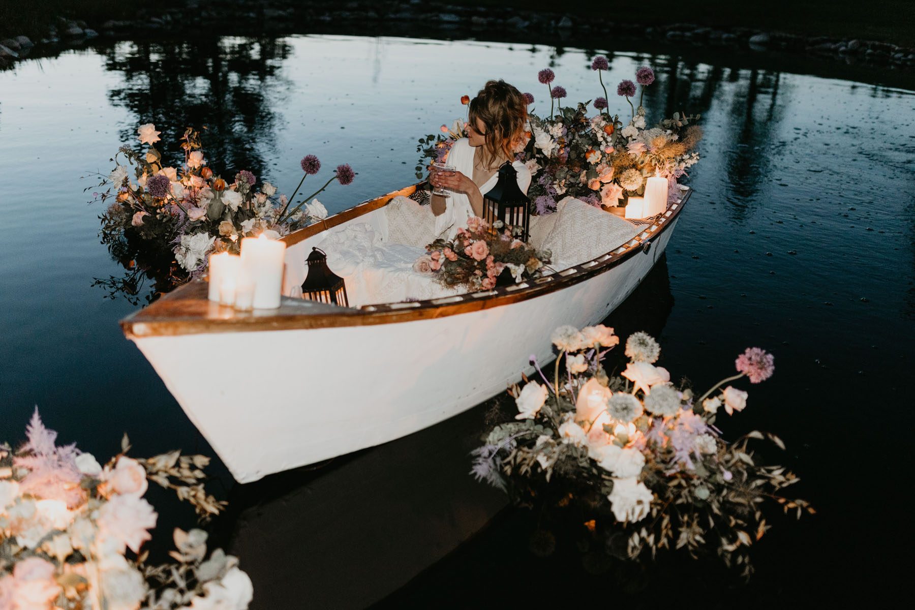 Moody floral photoshoot of woman in a canoe surrounded by candles and romantic floral arrangements
