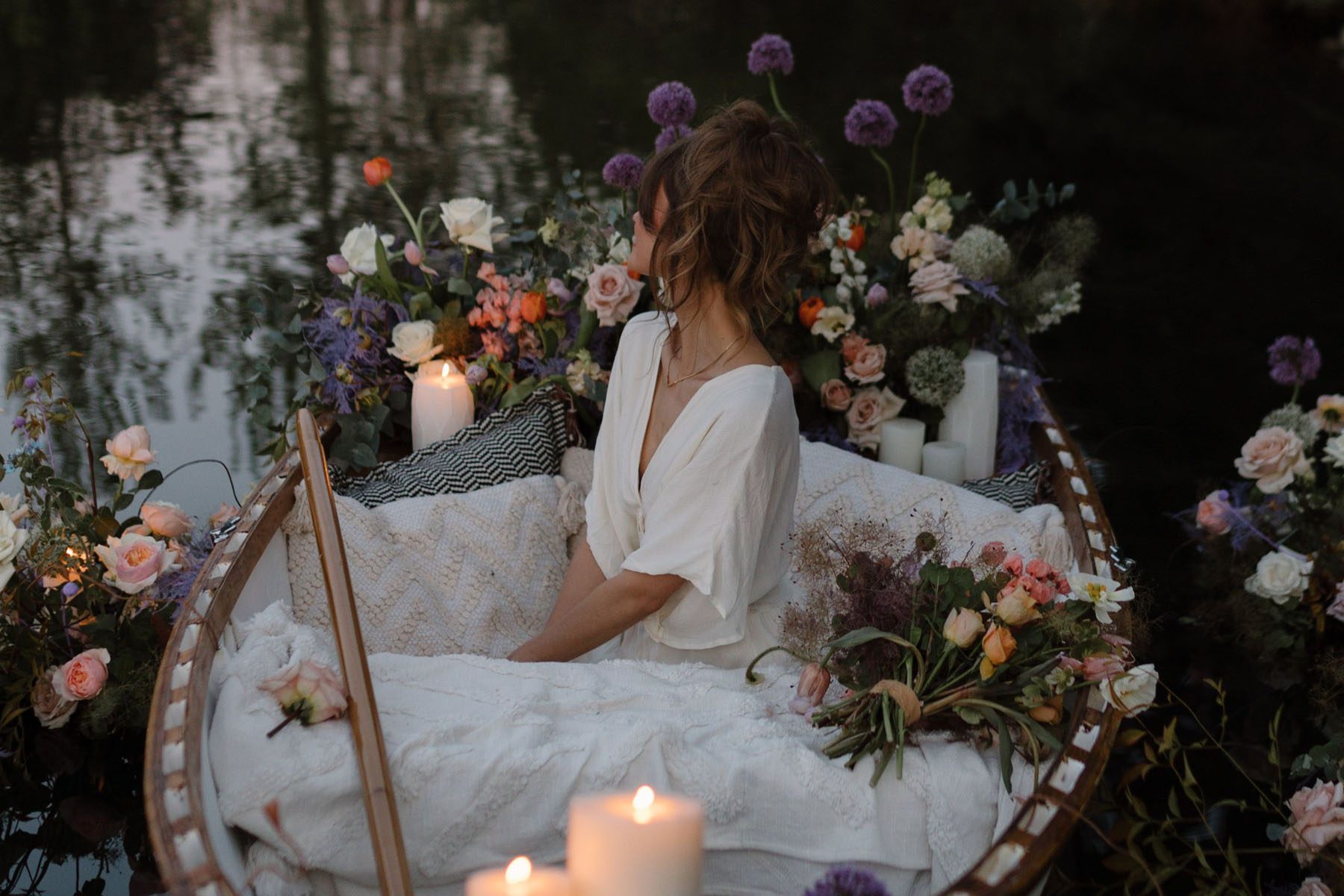 Candlelit florals surrounding woman in a canoe amongst pillows.