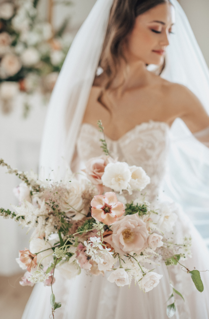 Bride holding a large wedding bouquet of blush, white flowers and minimal greenery.