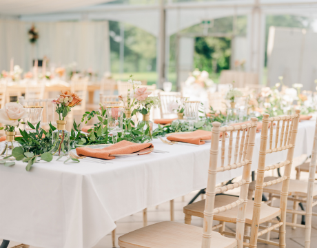 Event table draped with white linen with a row of delicate peach and blush flowers and greenery down the middle